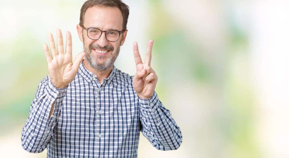 Man in a plaid shirt and glasses holding up seven fingers