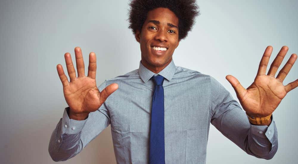 Man in a blue button-up shirt and blue tie holding up all ten of his fingers