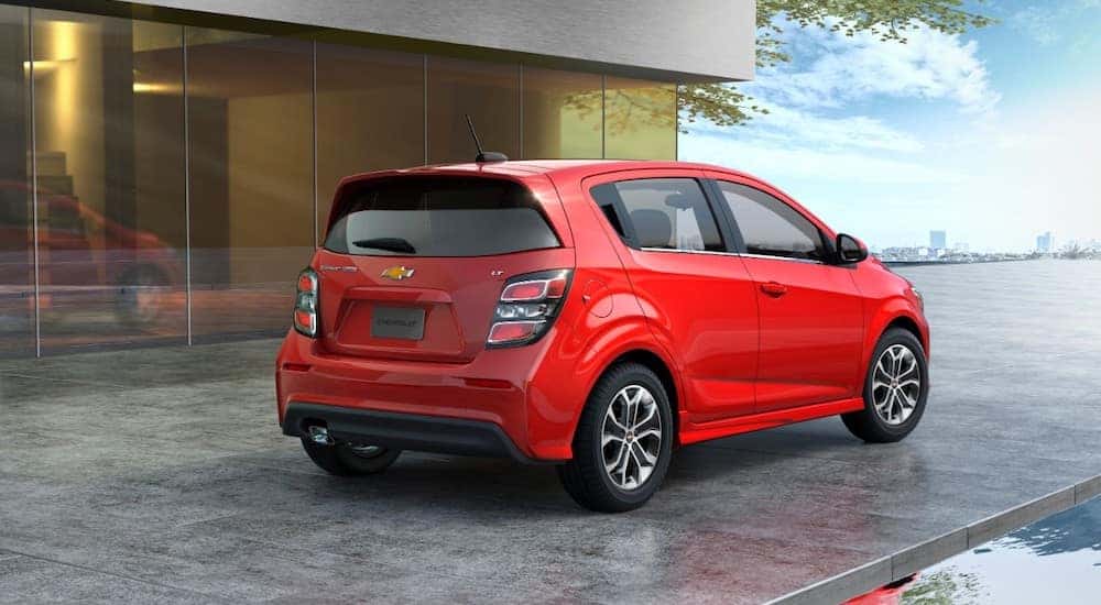 Red 2017 Chevrolet Sonic parked on a stone ground next to an all-glass building