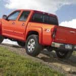 Orange 2010 Chevrolet Colorado Z71 driving up a hill on a dirt path next to green grass
