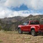 Red 2015 Chevrolet Silverado pickup truck parked in dirt in front of tall mountains and a cloudy sky