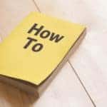 Yellow book with the title "How To" written on the front sitting on a wooden surface