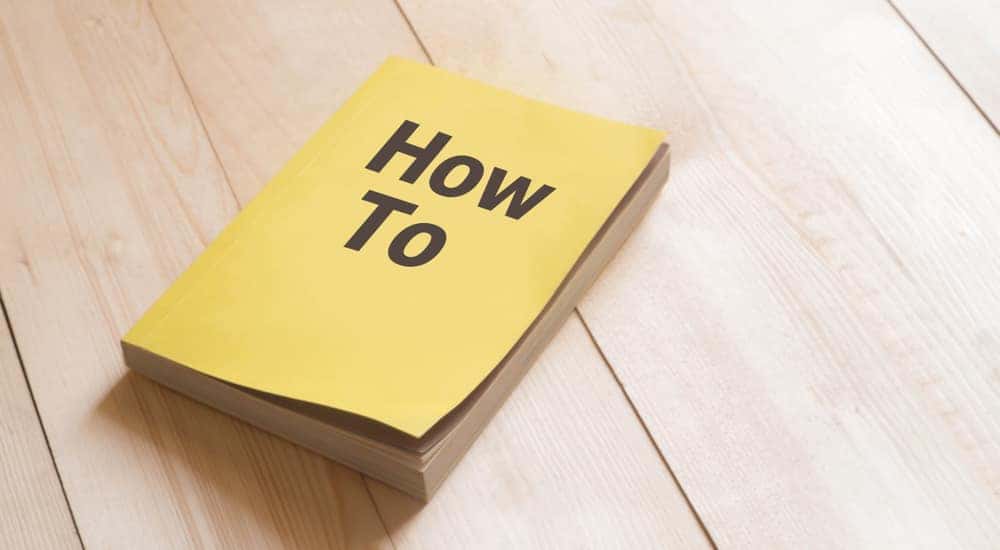 Yellow book with the title "How To" written on the front sitting on a wooden surface