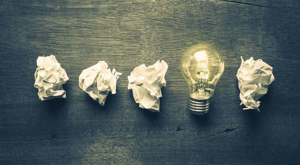 Four pieces of crumpled paper and a lit-up light bulb on a grey table