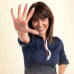 Woman in a blue button up shirt holding up five fingers against a yellow background