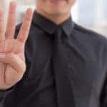 Man in a black button-up shirt and black tie holding four fingers up