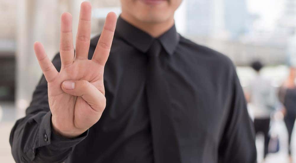 Man in a black button-up shirt and black tie holding four fingers up