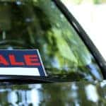 Black, red, and white "SALE" sign in the windshield of a black vehicle