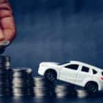 White toy car balanced on stacks of coins that are getting progressively taller