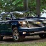 Blue 2018 Chevrolet Suburban driving up a dirt path path green grass and tall trees
