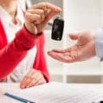 Salesperson handing a car key to a customer at a desk with a lease on it