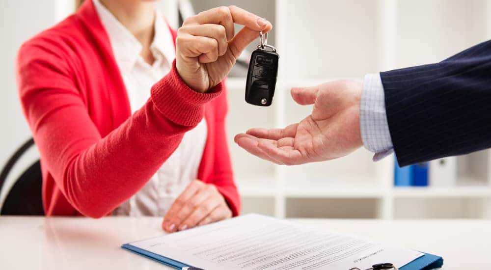 Salesperson handing a car key to a customer at a desk with a lease on it
