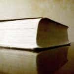 Large brown book with white pages sitting on a brown table in front of a tan wall