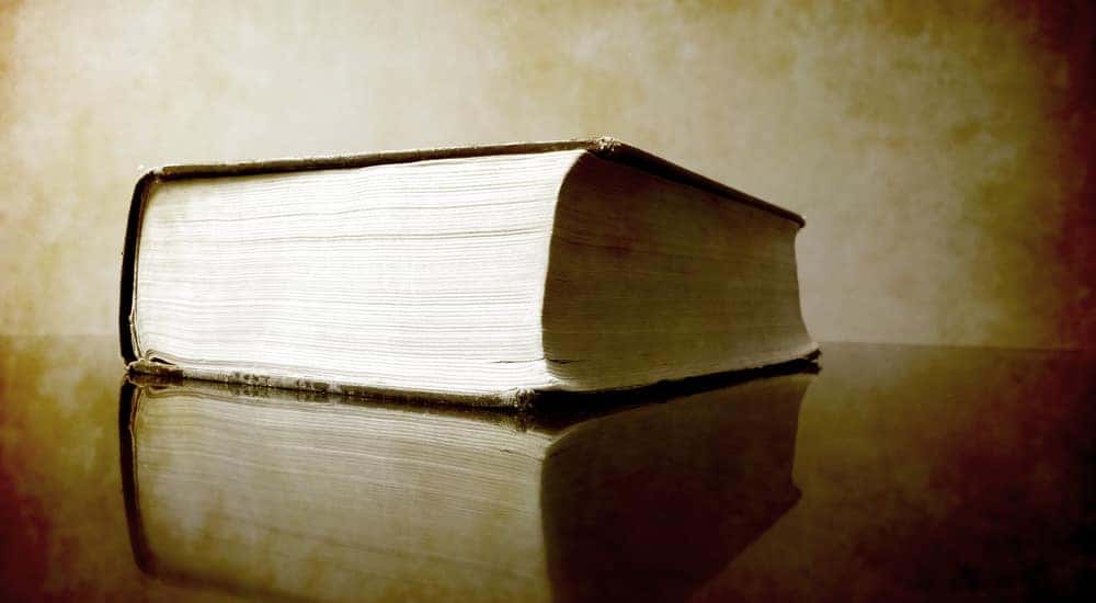 Large brown book with white pages sitting on a brown table in front of a tan wall