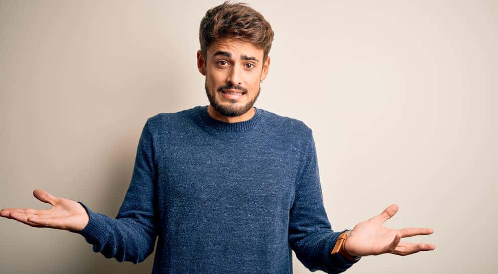 Man in a blue sweater shrugging in front of an off-white wall