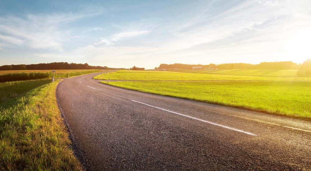 Long paved road with large grass fields on both sides and a blue sky above