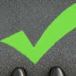 Bright green checkmark on the pavement in front of the toes of black shiny shoes