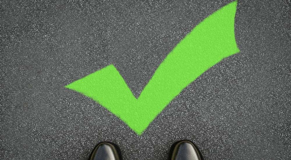 Bright green checkmark on the pavement in front of the toes of black shiny shoes
