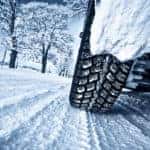 Tires driving on a snowy road with snowy trees and wispy clouds in the distance