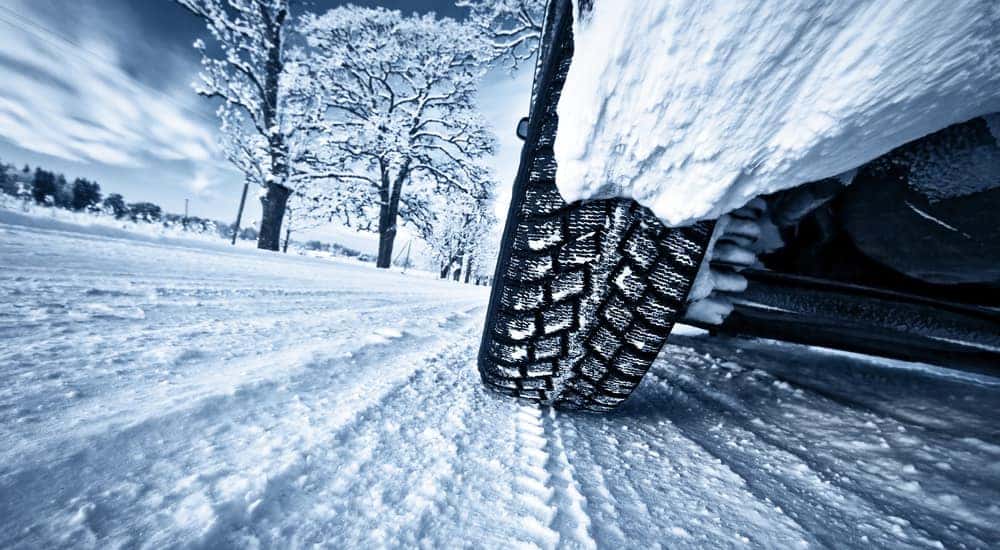 Tires driving on a snowy road with snowy trees and wispy clouds in the distance