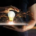Woman in a black shirt holding a tablet with a lightbulb and strings of fairy lights coming out of it