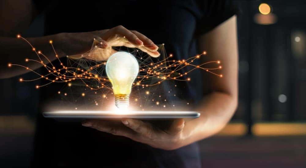Woman in a black shirt holding a tablet with a lightbulb and strings of fairy lights coming out of it
