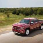 Red 2017 Chevrolet Silverado 1500 pickup truck driving down a paved road past green grass and trees