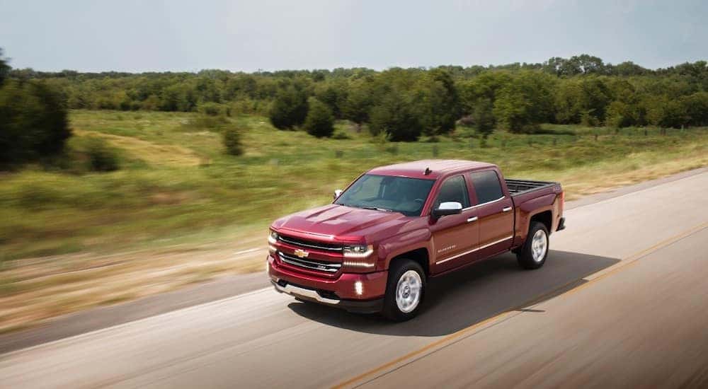 Red 2017 Chevrolet Silverado 1500 pickup truck driving down a paved road past green grass and trees