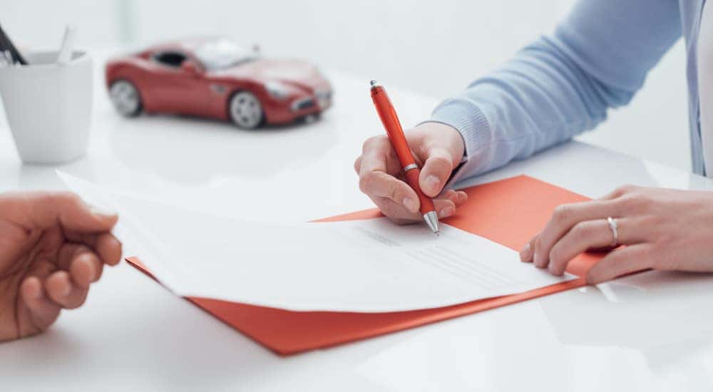 Hand holding a red pen and signing a car loan on a desk next to a red toy car