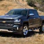 Black 2018 Chevrolet Silverado kicking up dust on a dirt path while driving past tall, brown grass
