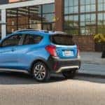 Light blue 2017 Chevrolet Spark hatchback parked on the side of a paved road in front of a brick building