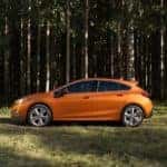 Orange 2018 Chevrolet Cruze hatchback parked on grass in front of tall, skinny trees
