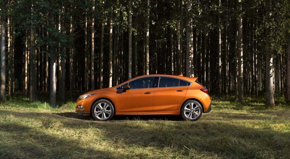 Orange 2018 Chevrolet Cruze hatchback parked on grass in front of tall, skinny trees