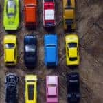 Various colors of toy cars next to one another in a rectangle formation on a wooden table