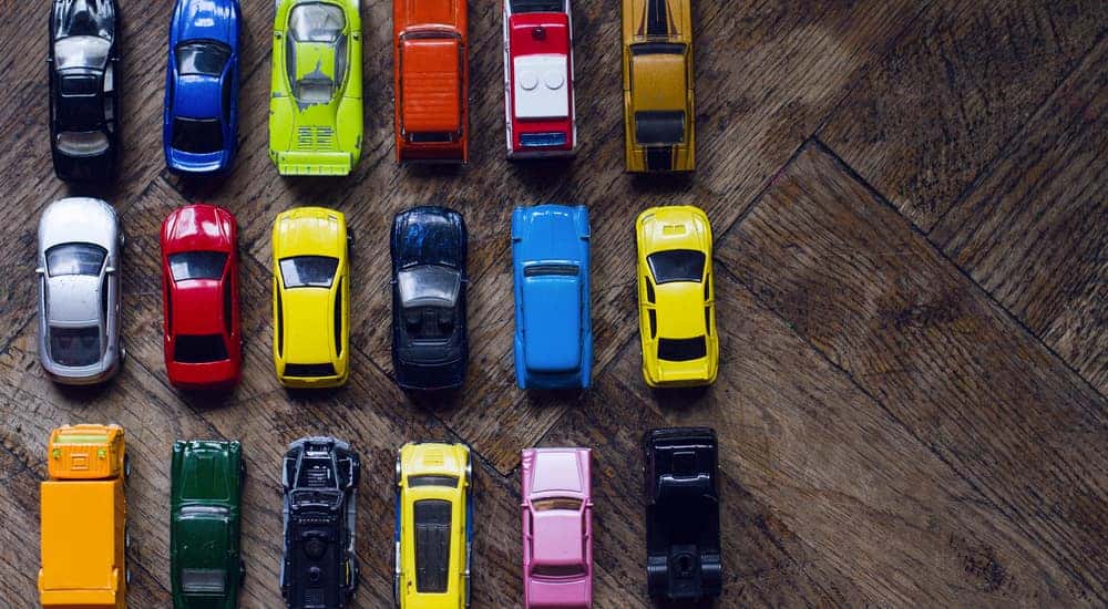 Various colors of toy cars next to one another in a rectangle formation on a wooden table