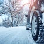 Vehicle driving down a snow covered road past snowy trees