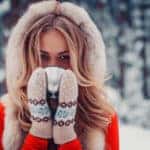 Woman in a red winter jacket and mittens drinking a hot drink in the snow