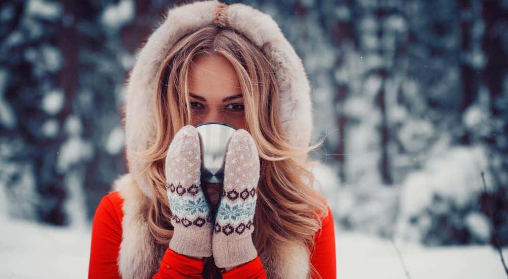 Woman in a red winter jacket and mittens drinking a hot drink in the snow