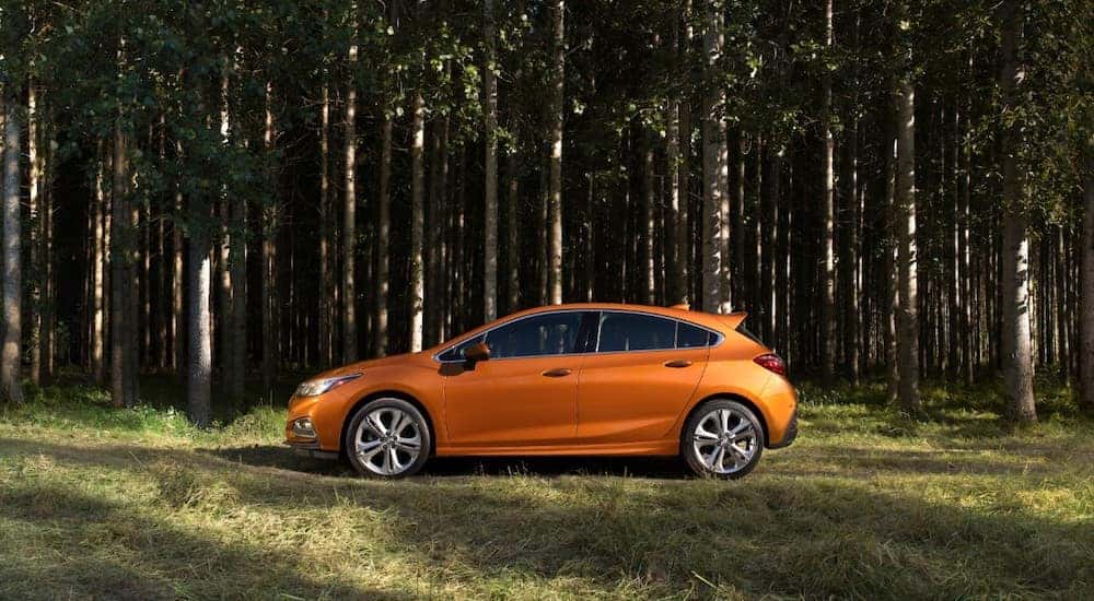 Orange 2018 Chevrolet Cruze Hatchback driving past green grass and tall, thin trees