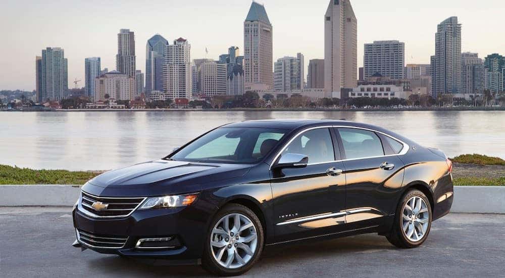 Black 2018 Chevrolet Impala sedan parked on cement in front of a large body of water and tall city buildings