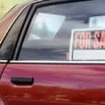 Orange, black, and white "FOR SALE" sign in the back passenger window of a red vehicle