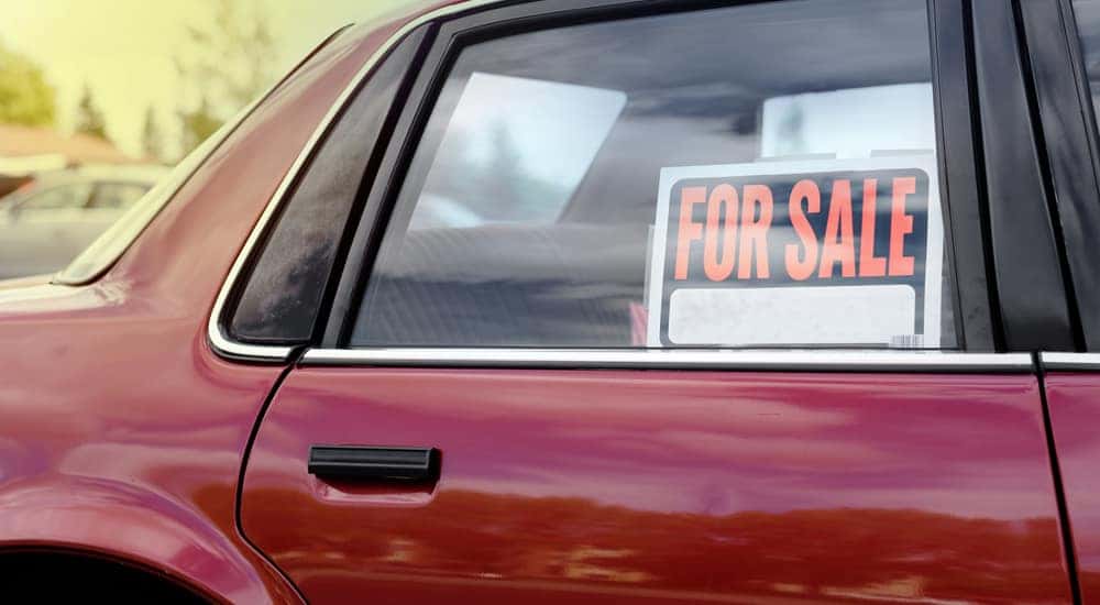 Orange, black, and white "FOR SALE" sign in the back passenger window of a red vehicle