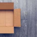 Open brown cardboard box sitting on a grey wooden floor