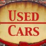 Yellow-brown sign with "USED CARS" and an arrow on it in red paint
