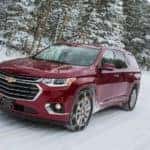 Maroon 2018 Chevrolet Traverse driving on a snowy road by pine trees