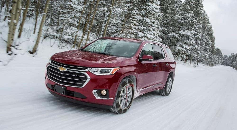 Maroon 2018 Chevrolet Traverse driving on a snowy road by pine trees