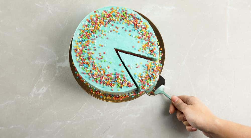 Hand using a spatula to take out a single slice of a blue cake with sprinkles all over it