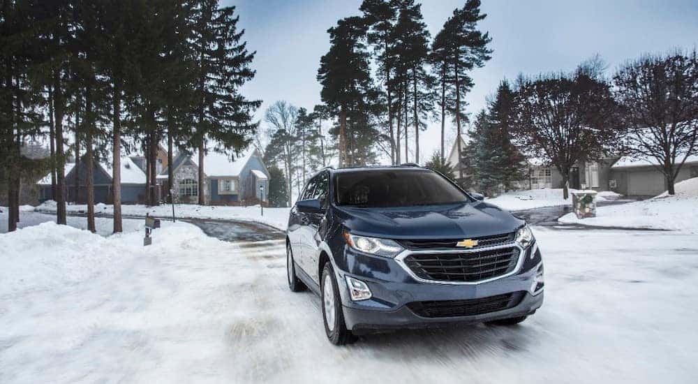 Blue 2018 Chevrolet Equinox driving down a snowy street through a neighborhood of houses