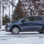 Blue 2018 Chevrolet Equinox SUV parked in the snow with trees in the background