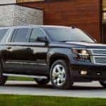 Black 2018 Chevrolet Suburban parked in front of a brown wood and grey stone house